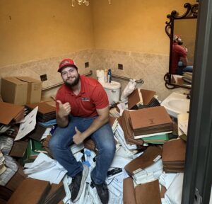 Junk Quest crew member surrounded by clutter and household junk before a full home cleanout and decluttering service — preparing for junk removal and organization.