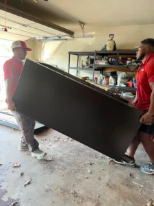 Junk Quest Removal team lifting and removing a large appliance from a garage in North Dallas