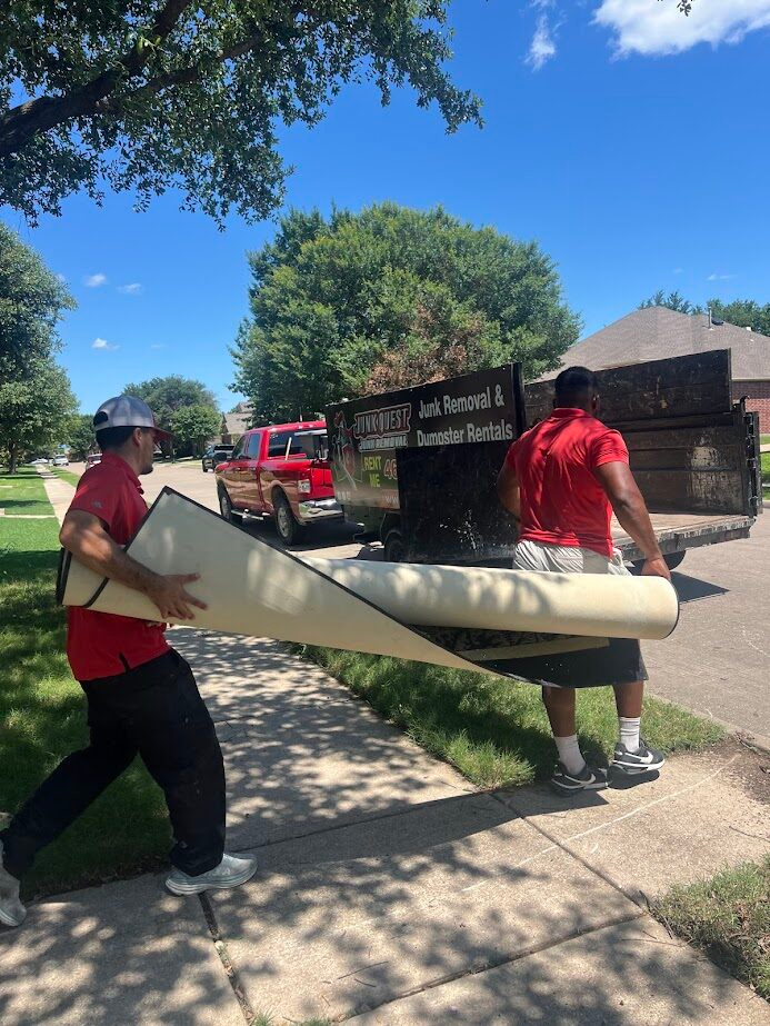 Junk Quest crew members carrying a rolled-up rug toward their trailer for disposal