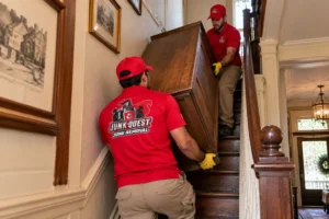 Junk removal crew maneuvering oversized furniture down a narrow stairwell in an older McKinney home